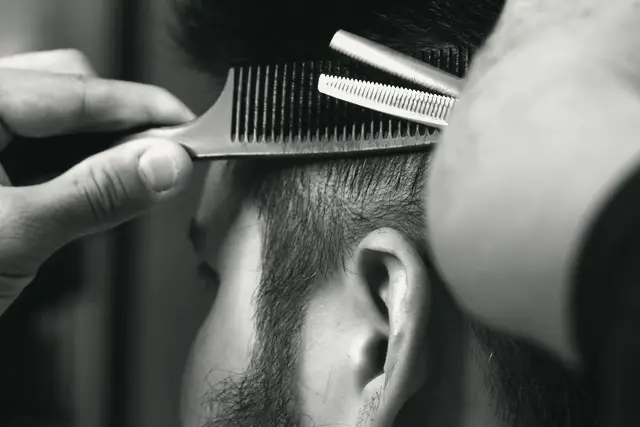 A barber using a comb and thinning shears on a client's hair