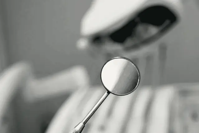 A dental mirror in the foreground with a dental chair behind it