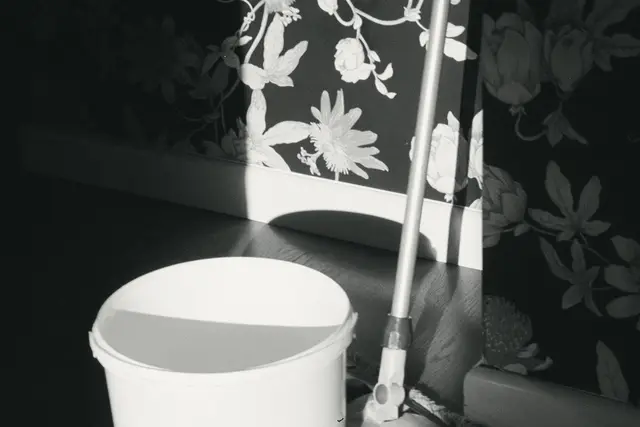 A white bucket and a mop against a wall