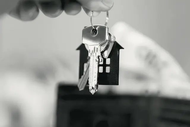 A hand holding house keys on a ring with a small house charm