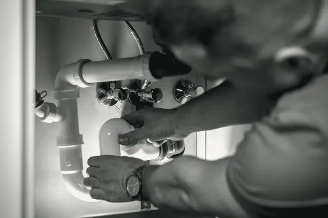 A plumber working on the pipes under a sink